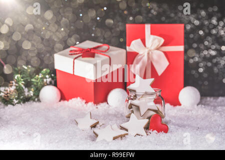 Pan di zenzero biscotti di Natale stelle nel vasetto di vetro e di doni in background con la neve. Copia dello spazio. Foto Stock