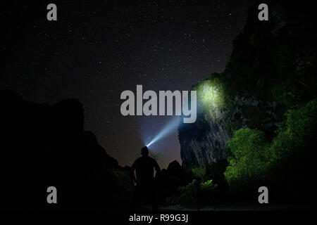 Silhouette di un uomo con un faro illuminazione di una scogliera in Laos durante la notte Foto Stock
