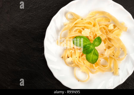 Un primo piano di un piatto di pasta italiana con parmigiano e di foglie di basilico fresco, ripresa dall'alto su sfondo scuro con un posto per il testo Foto Stock