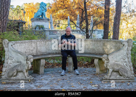 Berlino. Il vecchio uomo si siede sul banco decorartive nel giardino di casa della Conferenza di Wannsee Memorial sito con Flensburg Lion in background.. Foto Stock