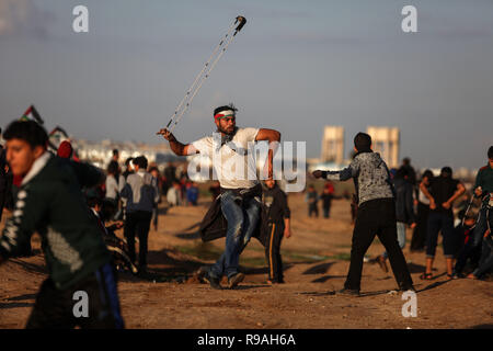 La striscia di Gaza, Territori palestinesi. Xxi Dec, 2018. Un manifestante palestinese utilizza una fionda di scagliare pietre contro le truppe israeliane sul confine Gaza-Israel, a est di Gaza City, il 21 dicembre, 2018. Un ragazzo palestinese è stato ucciso venerdì e almeno 40 altri feriti durante gli scontri tra dimostranti palestinesi e soldati israeliani nella parte orientale della striscia di Gaza, vicino alla frontiera con Israele, i medici hanno detto. Credito: Xinhua/Alamy Live News Foto Stock