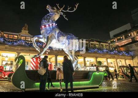 Londra, Regno Unito. 21 dic 2018. Una famiglia guardare una renna, parte delle luci di Natale a Covent Garden. I londinesi e turisti affollano il centro di Londra su che cosa è l'ultimo giorno lavorativo prima di Natale per molti nella capitale, e abbastanza mite serata a secco per la fine di dicembre. Credito: Imageplotter News e sport/Alamy Live News Foto Stock