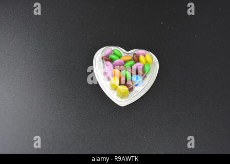 Combinazione con scatole d'argento sotto forma di cuori e cioccolatini multicolori in mezzo a loro, San Valentino, amore e gioia. Foto Stock