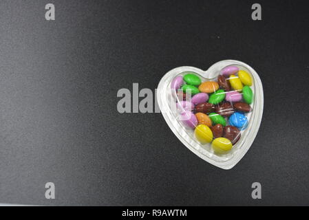 Combinazione con scatole d'argento sotto forma di cuori e cioccolatini multicolori in mezzo a loro, San Valentino, amore e gioia. Foto Stock