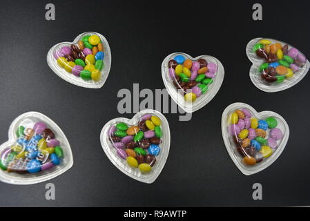 Combinazione con scatole d'argento sotto forma di cuori e cioccolatini multicolori in mezzo a loro, San Valentino, amore e gioia. Foto Stock