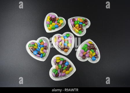 Combinazione con scatole d'argento sotto forma di cuori e cioccolatini multicolori in mezzo a loro, San Valentino, amore e gioia. Foto Stock