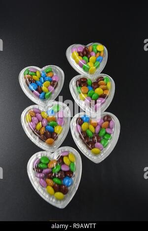 Combinazione con scatole d'argento sotto forma di cuori e cioccolatini multicolori in mezzo a loro, San Valentino, amore e gioia. Foto Stock