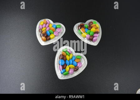 Combinazione con scatole d'argento sotto forma di cuori e cioccolatini multicolori in mezzo a loro, San Valentino, amore e gioia. Foto Stock