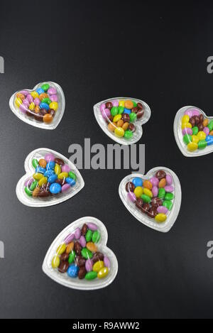 Combinazione con scatole d'argento sotto forma di cuori e cioccolatini multicolori in mezzo a loro, San Valentino, amore e gioia. Foto Stock