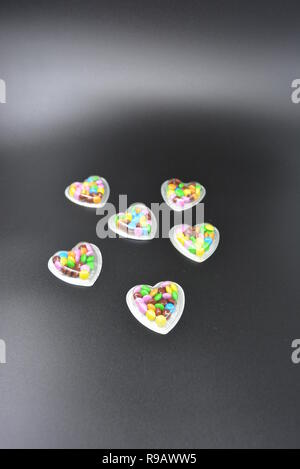 Combinazione con scatole d'argento sotto forma di cuori e cioccolatini multicolori in mezzo a loro, San Valentino, amore e gioia. Foto Stock