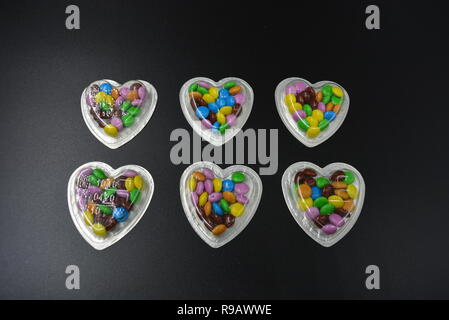 Combinazione con scatole d'argento sotto forma di cuori e cioccolatini multicolori in mezzo a loro, San Valentino, amore e gioia. Foto Stock