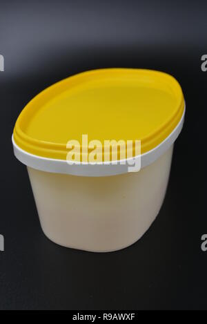 Contenitore in plastica bianco per alimenti e maionese con tappo giallo su sfondo nero elegante. Foto Stock