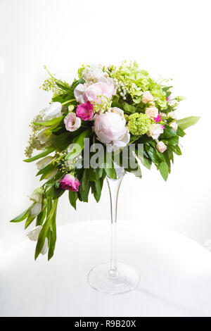 Un gran numero di yety, un grande mazzo di fiori lussureggianti della snowdrop, rosa, Campana e peonia con verdi in una grande lunga elegante vaso trasparente sulla gamba su un wh Foto Stock