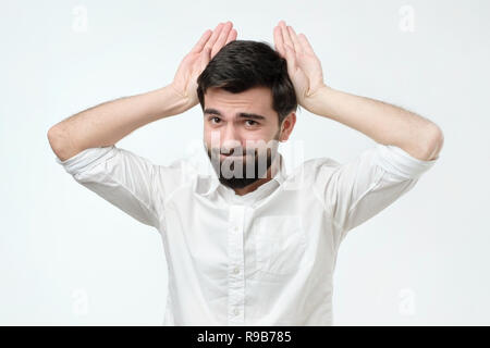 Carino divertente uomo ispanico con la barba, tenendo le mani in prossimità di testa come le orecchie animali Foto Stock