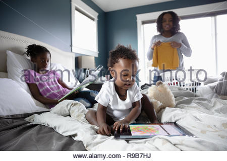 Madre di lavanderia di piegatura mentre i bambini leggere e giocare sul letto