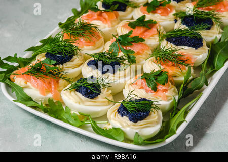 Uova ripiene con salmone e caviale decorate con il prezzemolo e l'aneto. Piatti per le feste Foto Stock