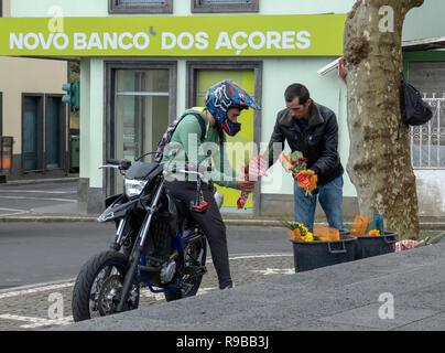 Moto Rider con il casco in testa si arresta per l'acquisto di un mazzo di fiori da un maschio di venditore ambulante davanti a 'Nuova Banca delle Azzorre " Foto Stock