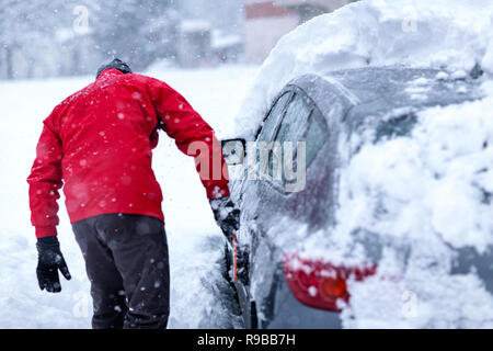 Giovane uomo pulizia vetri auto da neve nella stagione invernale Foto Stock