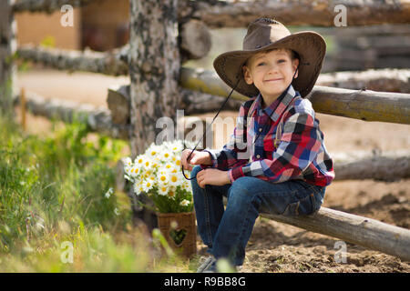 Carino fermer bello ragazzo cowboy in jeans godendo di giorno di estate in vita del villaggio con fiori in pelle da indossare mucca hat happyly sorridente Foto Stock