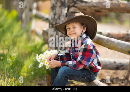 Carino fermer bello ragazzo cowboy in jeans godendo di giorno di estate in vita del villaggio con fiori in pelle da indossare mucca hat happyly sorridente Foto Stock