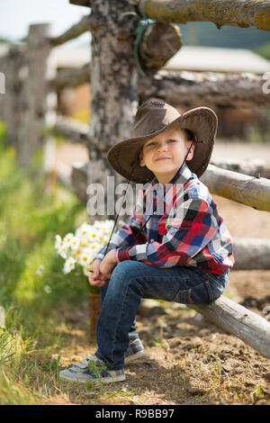 Carino fermer bello ragazzo cowboy in jeans godendo di giorno di estate in vita del villaggio con fiori in pelle da indossare mucca hat happyly sorridente Foto Stock