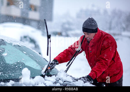 Spazzola in mano d'uomo. Giovane uomo cancella la neve ghiacciata dal parabrezza della vettura. Foto Stock