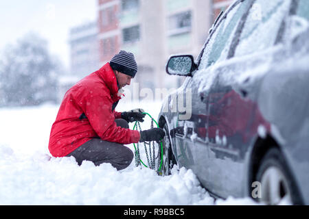 Giovane uomo installazione di catena da neve su auto Foto Stock