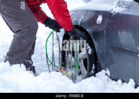 Giovane uomo cerca di mettere le catene da neve per pneumatici Foto Stock