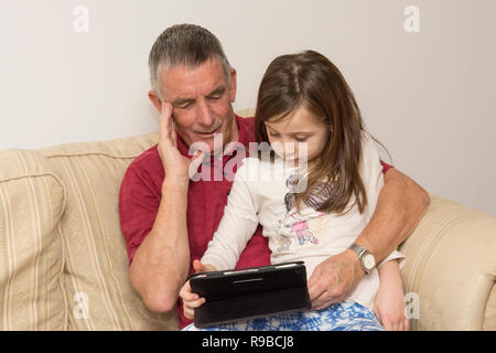 La nipote nonno aiuta con la compressa, dispositivo elettronico, social media, tecnologia moderna. ragazza aiutando il padre di invecchiamento con iPad, tablet. Foto Stock