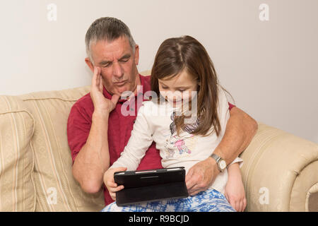 La nipote nonno aiuta con la compressa, dispositivo elettronico, social media, tecnologia moderna. ragazza aiutando il padre di invecchiamento con iPad, tablet. Foto Stock