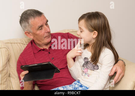 La nipote nonno aiuta con la compressa, dispositivo elettronico, social media, tecnologia moderna. ragazza aiutando il padre di invecchiamento con iPad, tablet. Foto Stock