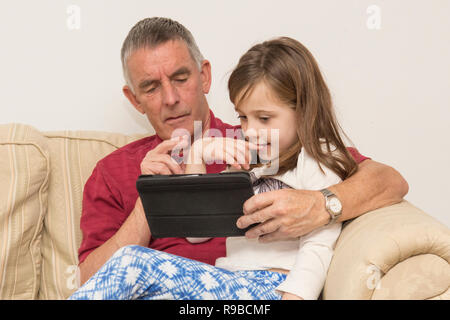 La nipote nonno aiuta con la compressa, dispositivo elettronico, social media, tecnologia moderna. ragazza aiutando il padre di invecchiamento con iPad, tablet. Foto Stock