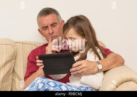 La nipote nonno aiuta con la compressa, dispositivo elettronico, social media, tecnologia moderna. ragazza aiutando il padre di invecchiamento con iPad, tablet. Foto Stock