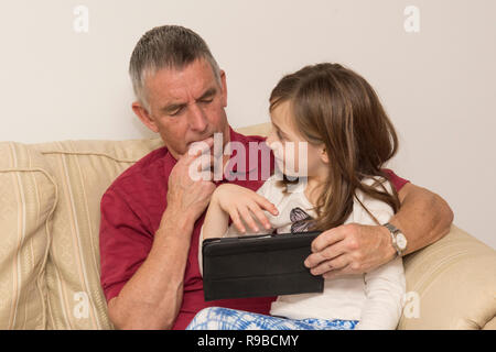 La nipote nonno aiuta con la compressa, dispositivo elettronico, social media, tecnologia moderna. ragazza aiutando il padre di invecchiamento con iPad, tablet. Foto Stock