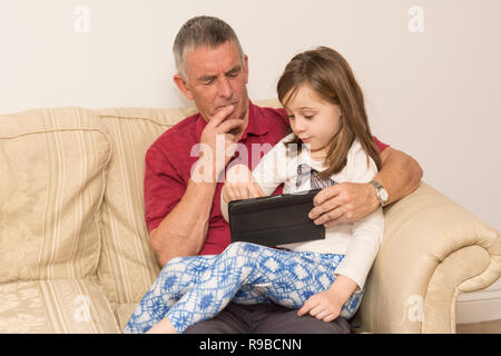 La nipote nonno aiuta con la compressa, dispositivo elettronico, social media, tecnologia moderna. ragazza aiutando il padre di invecchiamento con iPad, tablet. Foto Stock