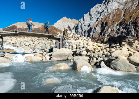 Il trekking attraversando ponte di legno su un fiume glaciale sul circuito di Manaslu Trek, Nepal Himalaya Foto Stock