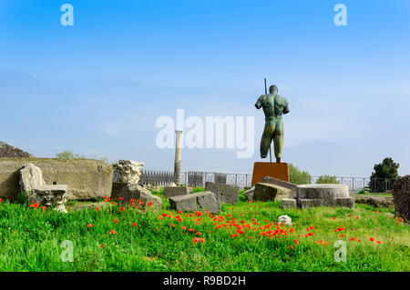 Scavi di Pompei e la statua in bronzo di Daedalus da Igor Mitoraj tra i papaveri e l'erba verde. Sito archeologico di Pompei antica città distrutta da er Foto Stock