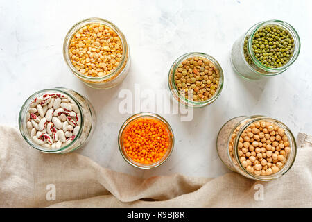 Un assortimento di legumi secchi e legumi in vetro vasi da cucina vista dal di sopra con piselli, lenticchie, fagioli, ceci, su un panno bianco Foto Stock