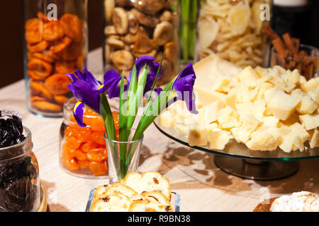 Closeup snack, frutta secca e noci in recipiente di vetro, iridi di fiori in vaso, piastra con pezzi di formaggio parmigiano. Concetto di lusso degustazione banque Foto Stock