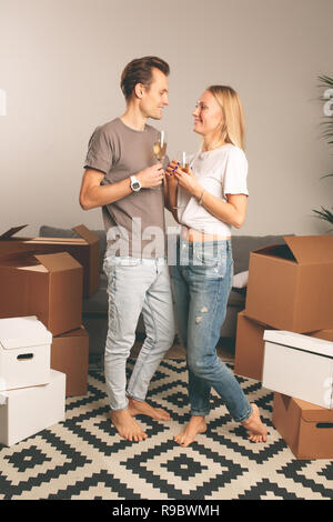 Immagine della coppia felice con bicchieri di vino in piedi tra le scatole di cartone Foto Stock