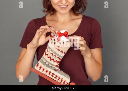 Giovane donna in piedi isolato sul muro grigio messa piccola confezione regalo nella calza decorata sorridente allegro close-up Foto Stock