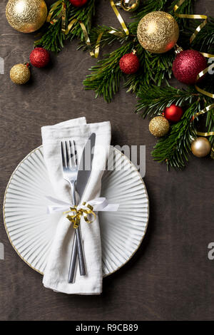 Cena di Natale tavola con piastra bianca, forcella, coltello e igienico, Natale decorazioni di festa intorno a. Tradizionali decorazioni di Natale. Romantico set di tavola Foto Stock