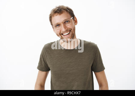 Gioiosa amichevole-cercando carino brunet con setola in bicchieri e verde scuro e t-shirt testa tiltante avente bella interessante conversazione sorridendo ampiamente godendo divertente parlare oltre il muro grigio Foto Stock