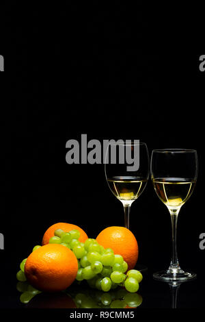 Tre Bicchieri per il vino, un grappolo di uva e arance su uno sfondo nero, studio luce Foto Stock