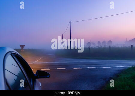 Macchina arrestata in corrispondenza di un incrocio in Orne campagna in una serata di nebbia al blue ora, Normandia Francia Foto Stock