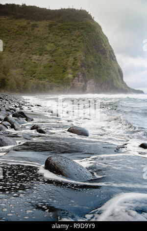 Onde che si infrangono sulle rocce sulla spiaggia nella valle Waipio sulla Big Island delle Hawaii. Foto Stock