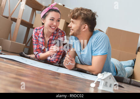Giovane marito e moglie di passare a nuovo luogo sdraiato sul pavimento afferrando i bicchieri di vino rosso cheers parlando sorridente gioiosa Foto Stock