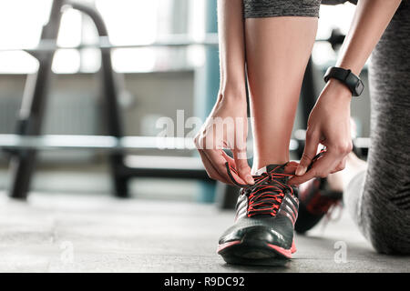 Giovane donna in palestra uno stile di vita sano in piedi sul ginocchio holding lacci delle scarpe rendendo sulla prua sneakers su un piede di close-up Foto Stock