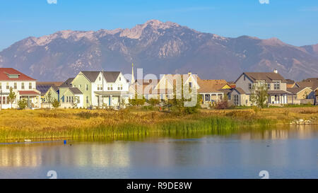 Case e lago riflettente con sfondo di montagna Foto Stock