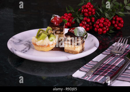 Tiny tortina con kiwi, panna montata e torta al cioccolato su un marmo nero tabella Foto Stock